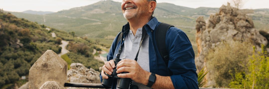 Older man in nature smiling holding binoculars 
