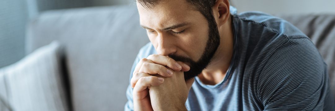 Stressed man putting chin on folded hands 