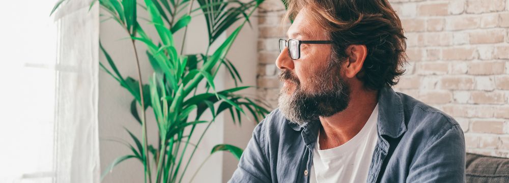 Middle age man with glasses looking out window on sunny day 